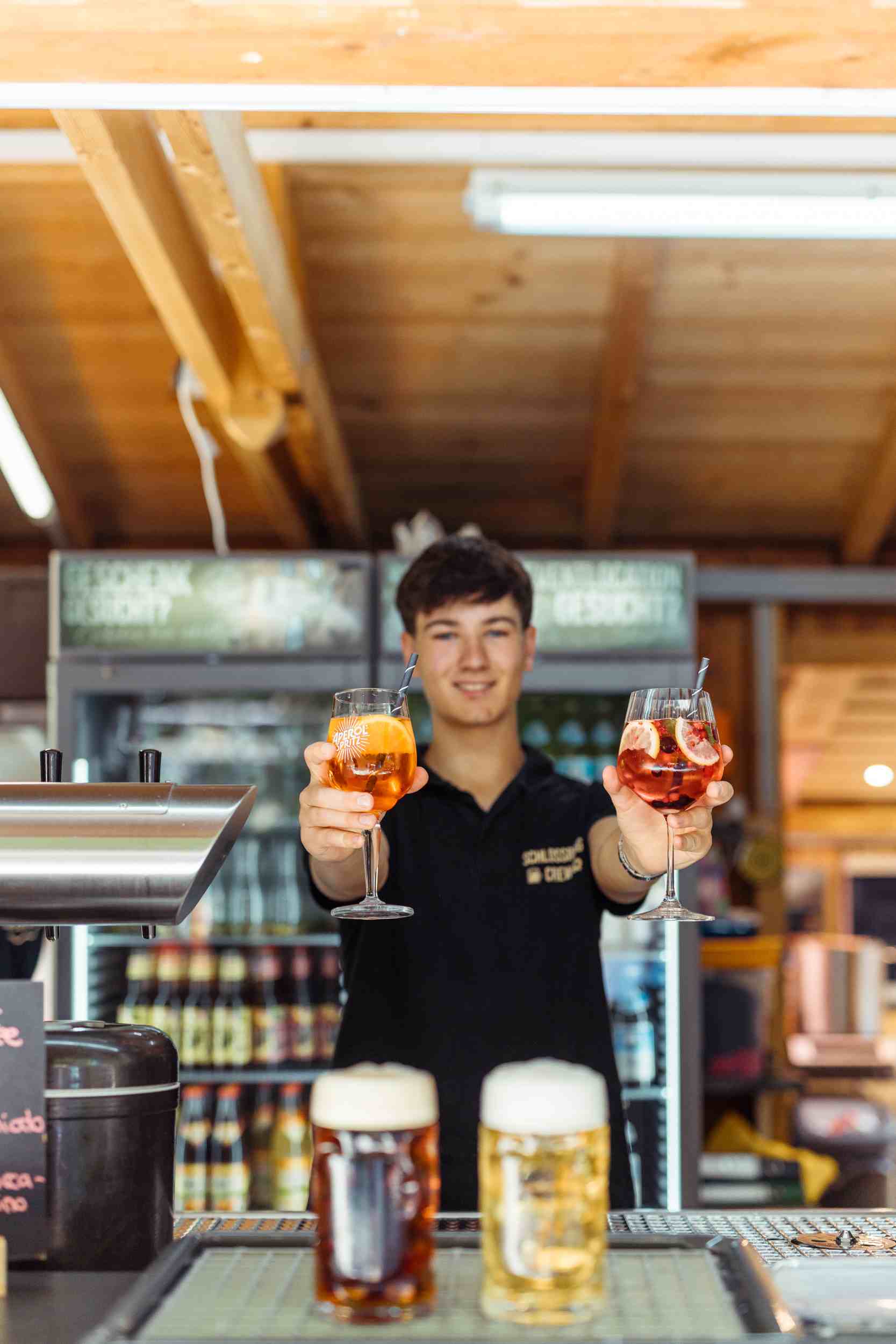 Mitarbeiter präsentiert zwei sommerliche Aperol-Drinks an der Bar